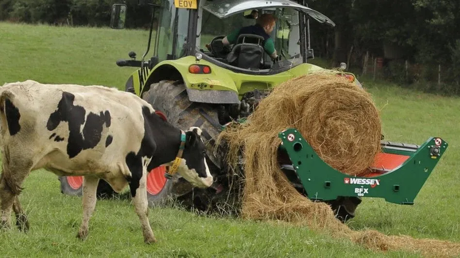 A tractor in a field using a piece Wessex International equipment hitched on the back to feed hay to the cows in the field