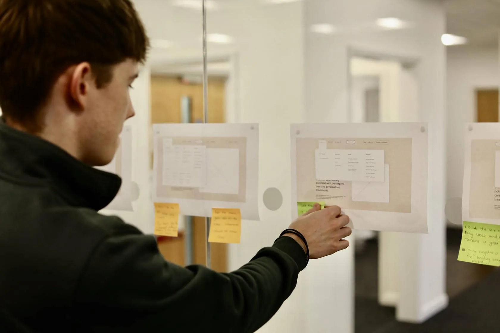 A UX designer placing sticky notes onto printed website navigation wireframes