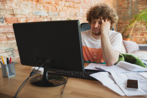 A man sat at a desk, looking at his computer, frustrated with a website's site speed.