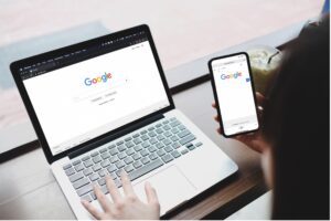 A woman using her Apple Macbook laptop and iPhone to search Google simultaneously.
