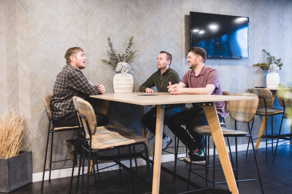 Three members of Damteq's client service team sat at a wooden table in a modern office having a conversation