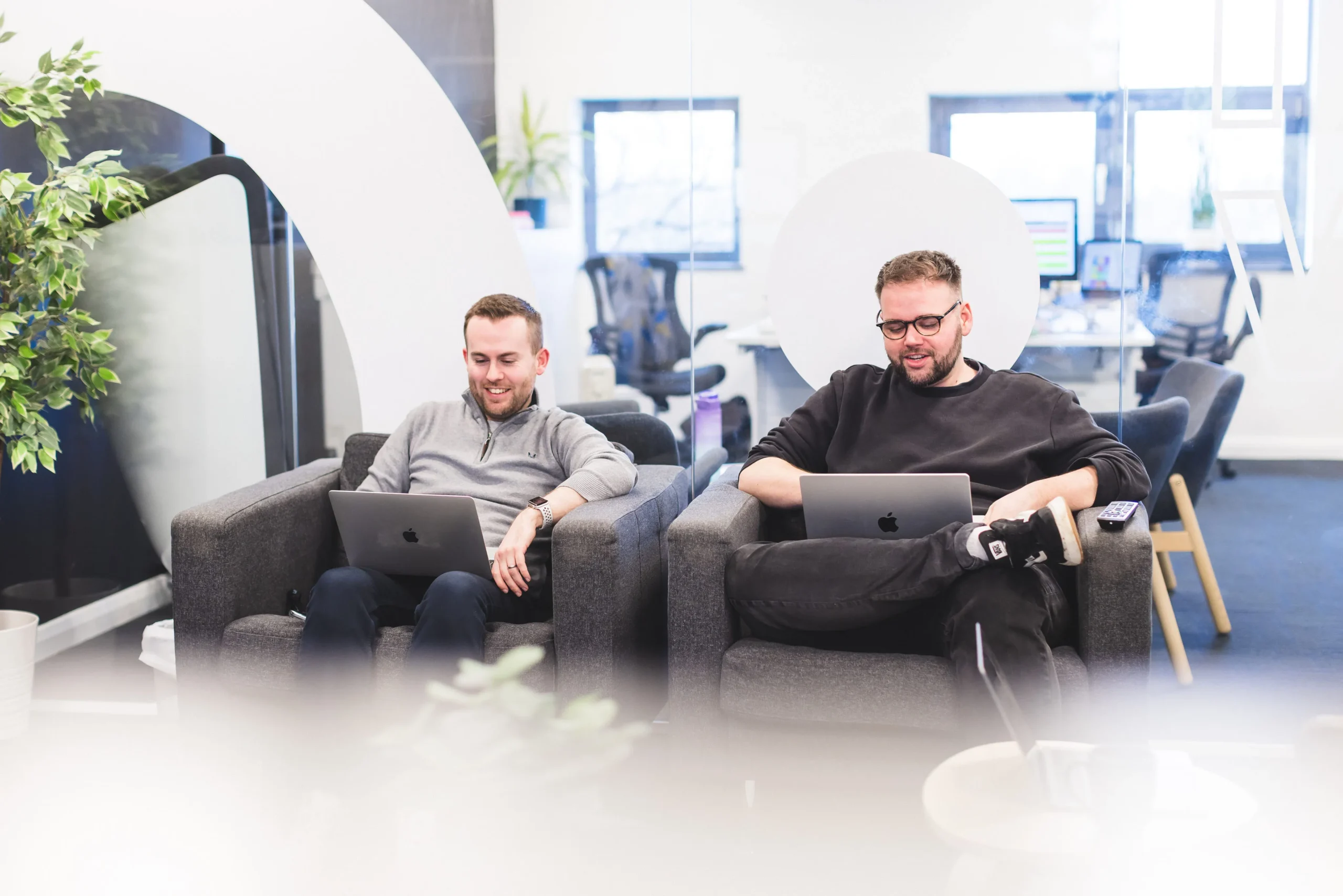 Josh Drew and Adam Flood sat on office sofas, working on their laptops