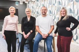 Four members of Damteq's management team stood in a boardroom, smiling and looking at the camera