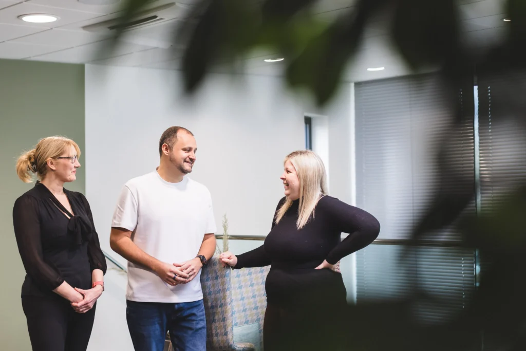 Adam, Sarah, and Lisa, stood talking in the Damteq office