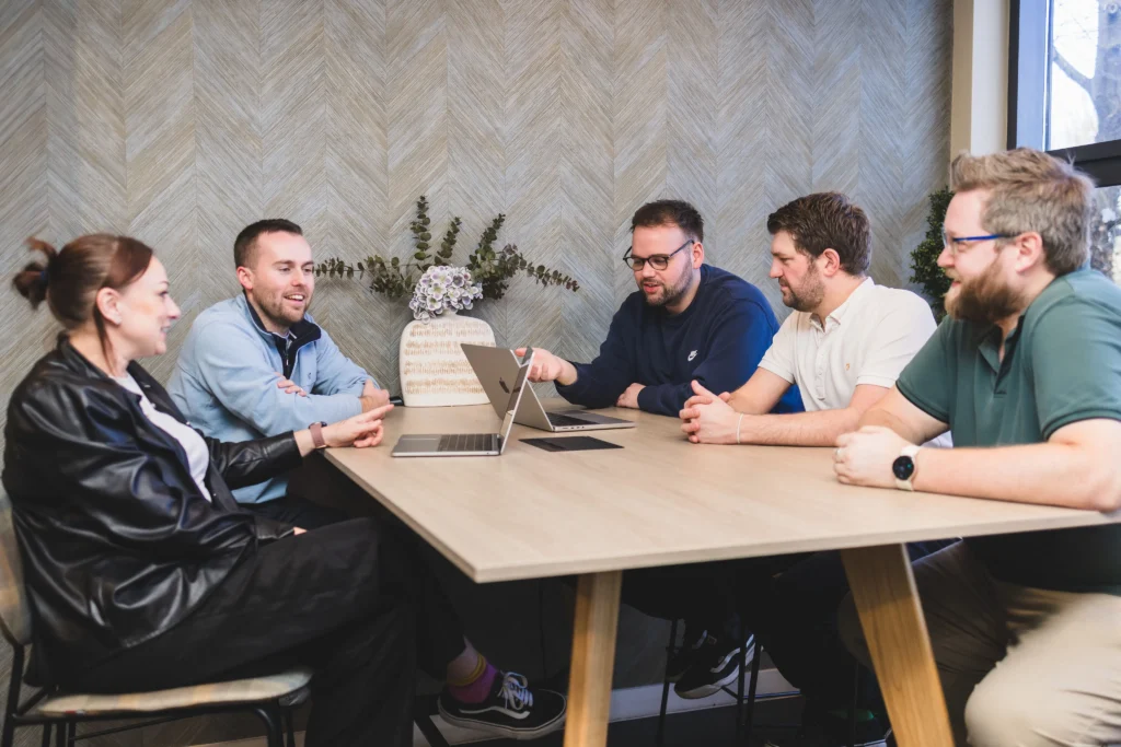 Damteq's Marketing and Web Specialists collaborating around two laptops on a table.